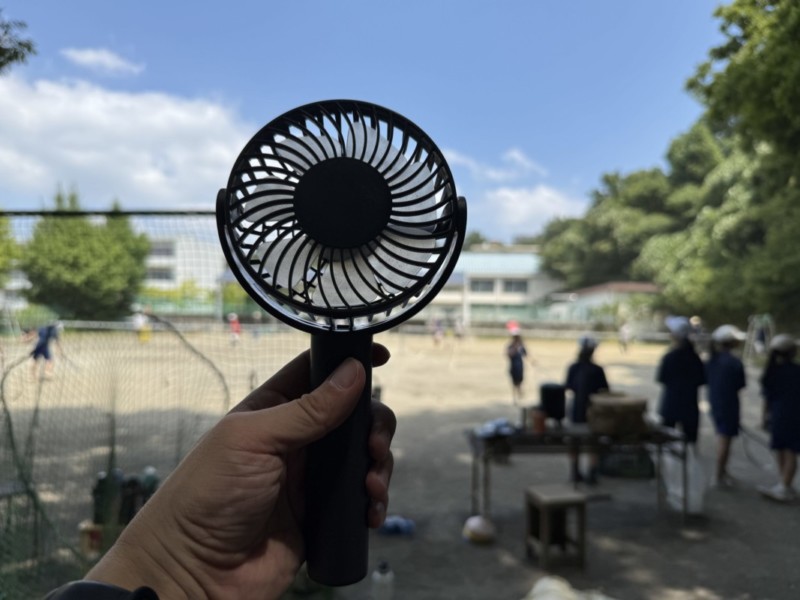 テニス部の練習風景を背景にハンディファンを撮影した画像