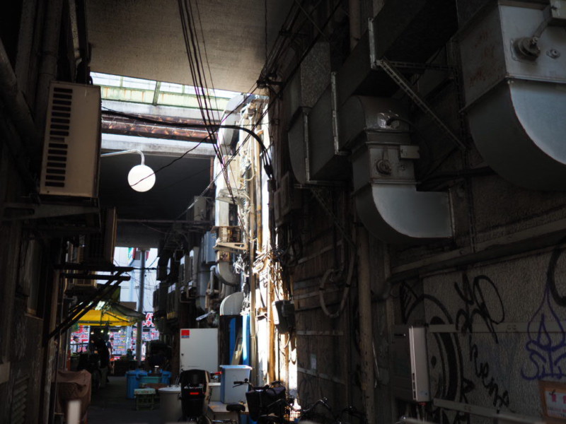 アメ横の路地裏の写真、換気口・ダクト・配線が入り乱れた薄暗い通り