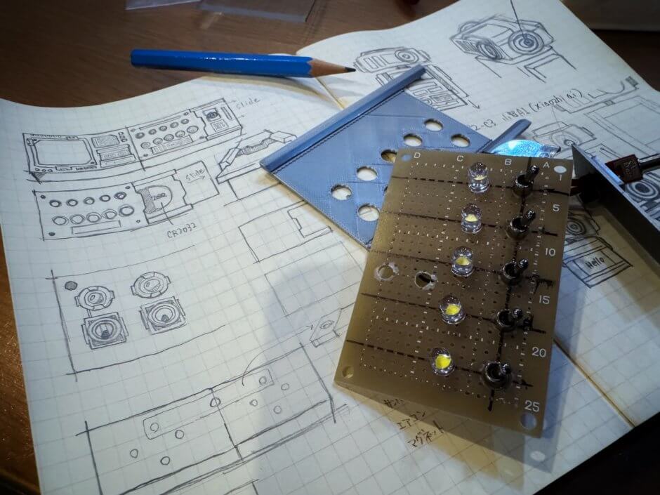 3Dプリンター新商品開発中のアイデアスケッチと電子基板が机に散乱している写真